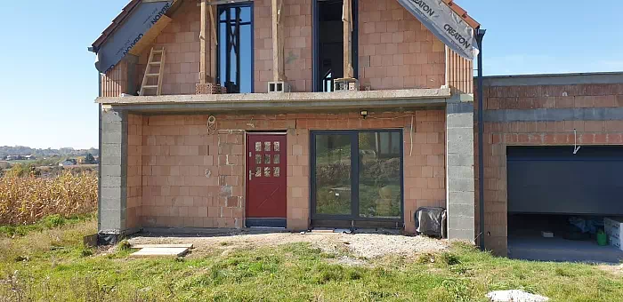Widok elewacji domu z zamontowanymi drzwiami wzór 507,5 wymalowanymi w kolorze czerwone.