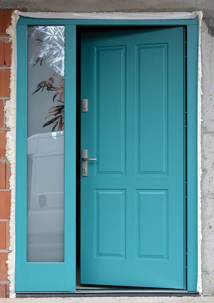 Widok elewacji domu z zamontowanymi drzwiami wzór 534,9 wymalowanymi w kolorze błękitne.
