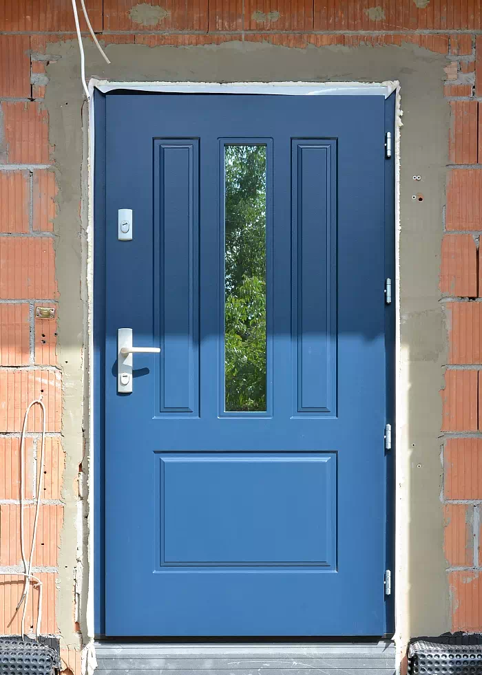 Widok elewacji domu z zamontowanymi drzwiami wzór 555,2 wymalowanymi w kolorze niebieskie.