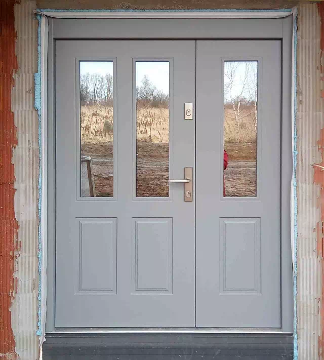 Widok elewacji domu z zamontowanymi drzwiami wzór 534,9B wymalowanymi w kolorze szare.
