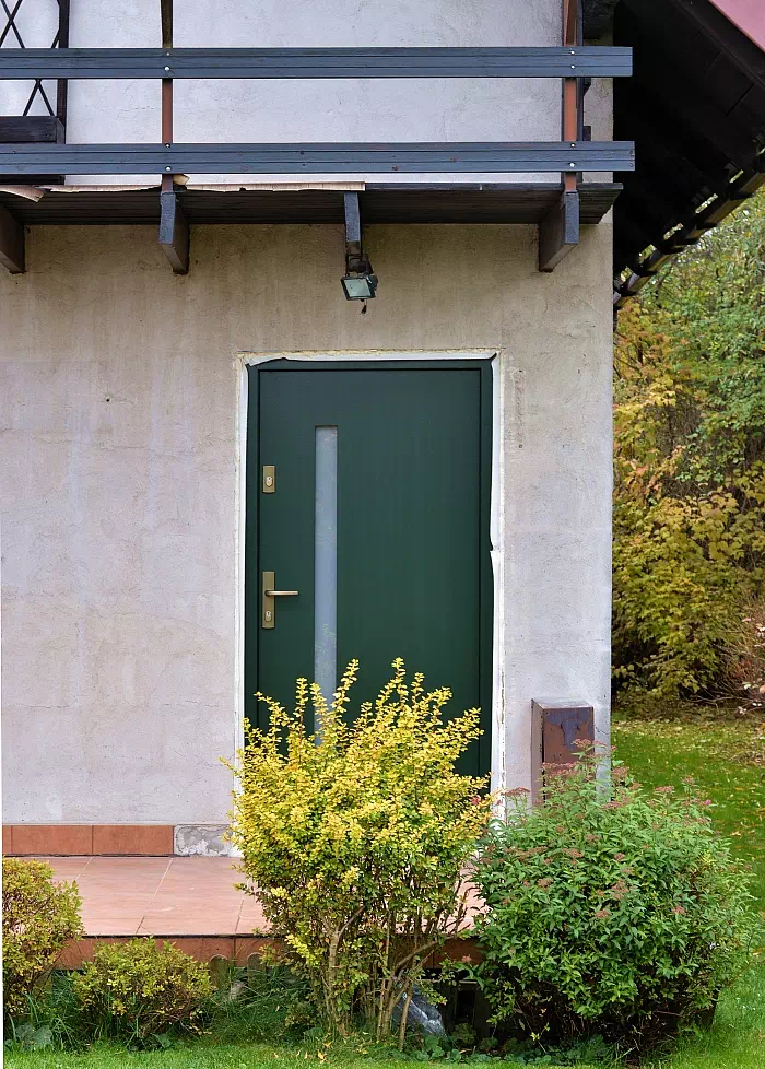 Widok elewacji domu z zamontowanymi drzwiami wzór 417,11 wymalowanymi w kolorze zielone.