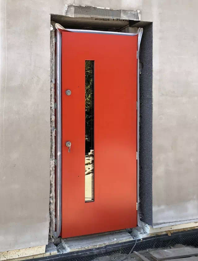 Widok elewacji domu z zamontowanymi drzwiami wzór 427,13 wymalowanymi w kolorze czerwone.