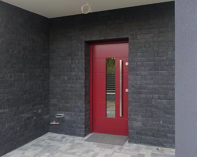 Widok elewacji domu z zamontowanymi drzwiami wzór 466,5 wymalowanymi w kolorze czerwone.