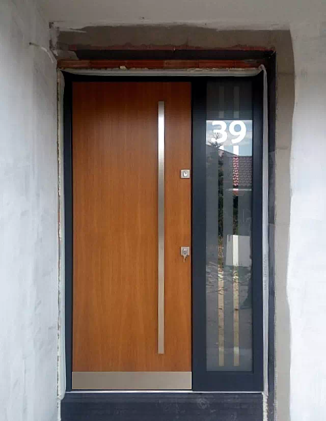 Widok elewacji domu z zamontowanymi drzwiami wzór 500C wymalowanymi w kolorze dąb średni.