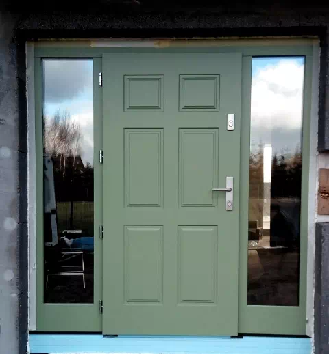 Widok elewacji domu z zamontowanymi drzwiami wzór 533,10 wymalowanymi w kolorze zielone.