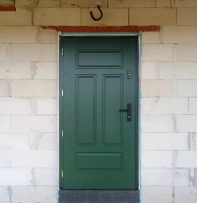 Widok elewacji domu z zamontowanymi drzwiami wzór 533,12 wymalowanymi w kolorze zielone.