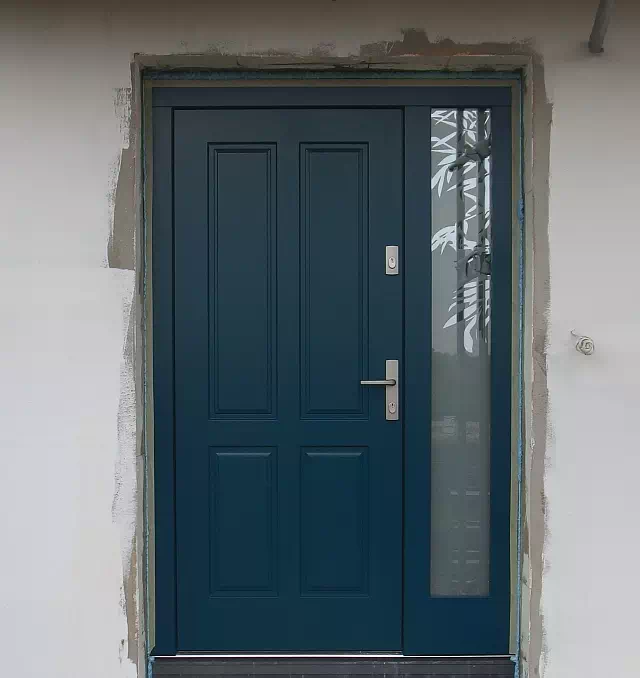 Widok elewacji domu z zamontowanymi drzwiami wzór 534,9 wymalowanymi w kolorze granatowe.