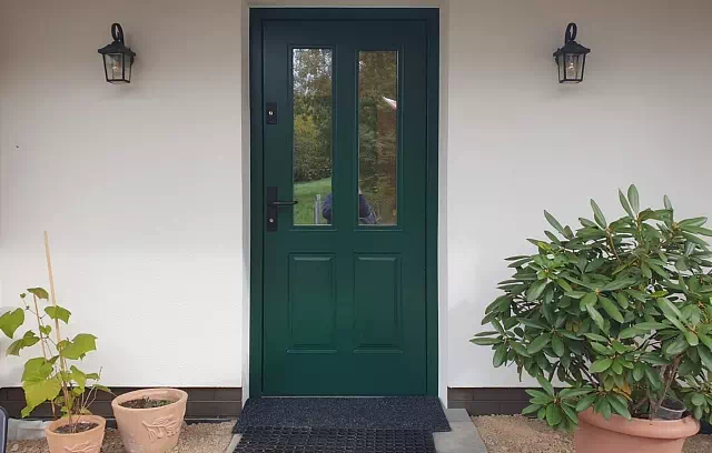 Widok elewacji domu z zamontowanymi drzwiami wzór 534,9b wymalowanymi w kolorze zielone.