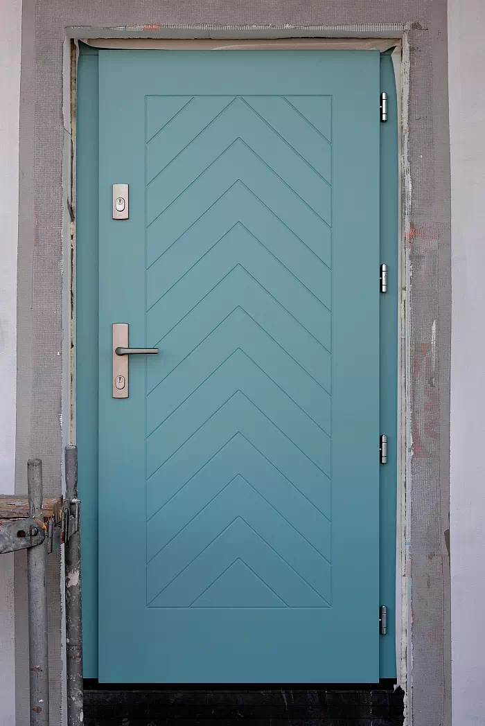 Widok elewacji domu z zamontowanymi drzwiami wzór 543,2 wymalowanymi w kolorze turkusowe.