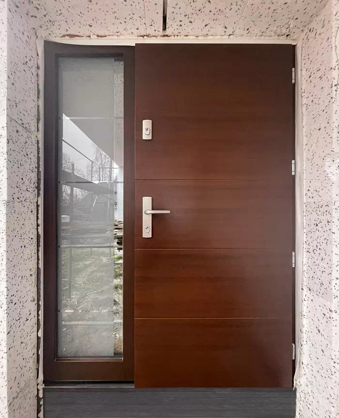 Widok elewacji domu z zamontowanymi drzwiami wzór 490,15B wymalowanymi w kolorze orzech.