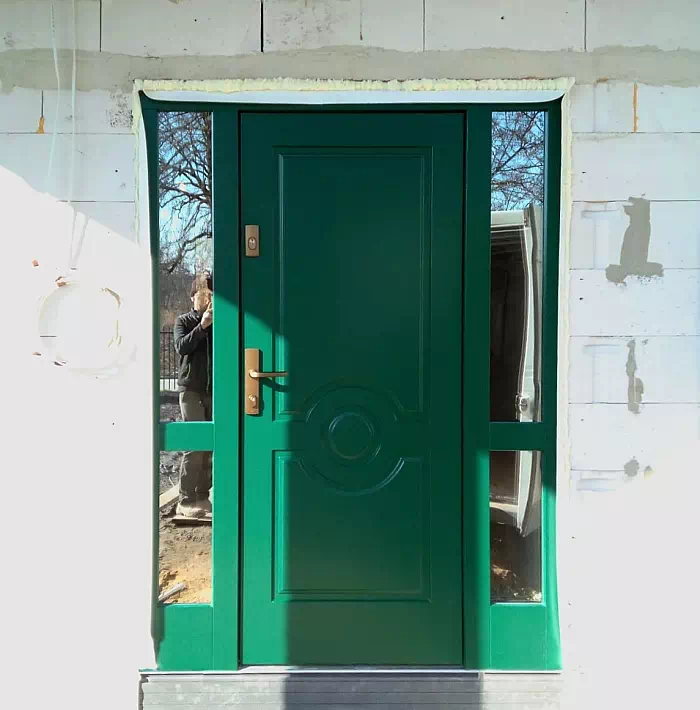 Widok elewacji domu z zamontowanymi drzwiami wzór 504,1 wymalowanymi w kolorze zielone.