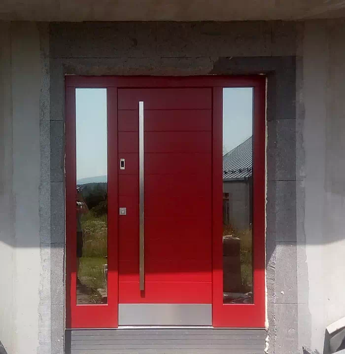 Widok elewacji domu z zamontowanymi drzwiami wzór 431,1 wymalowanymi w kolorze czerwone.