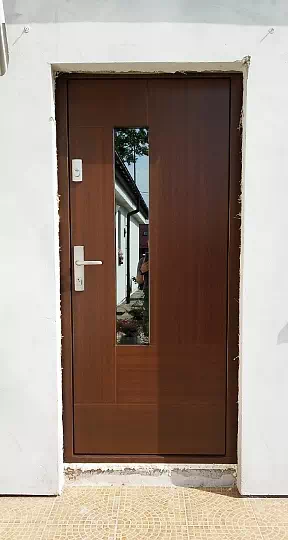 Widok elewacji domu z zamontowanymi drzwiami wzór 413,11C wymalowanymi w kolorze orzech.