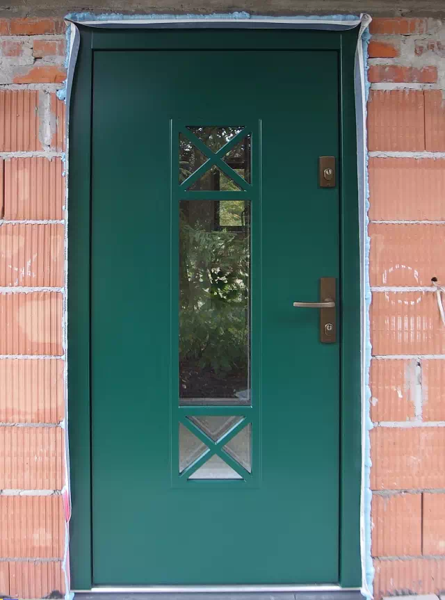 Widok elewacji domu z zamontowanymi drzwiami wzór 461,1 wymalowanymi w kolorze zielone.