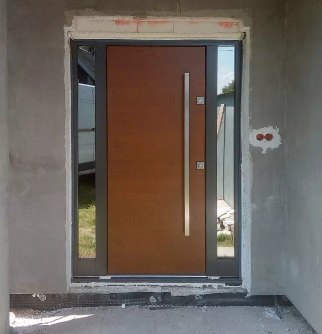 Widok elewacji domu z zamontowanymi drzwiami wzór 500C wymalowanymi w kolorze ciemny dąb + antracyt.