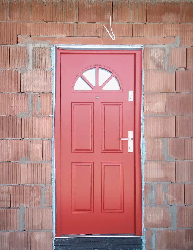 Widok elewacji domu z zamontowanymi drzwiami wzór 506,2 wymalowanymi w kolorze czerwone.