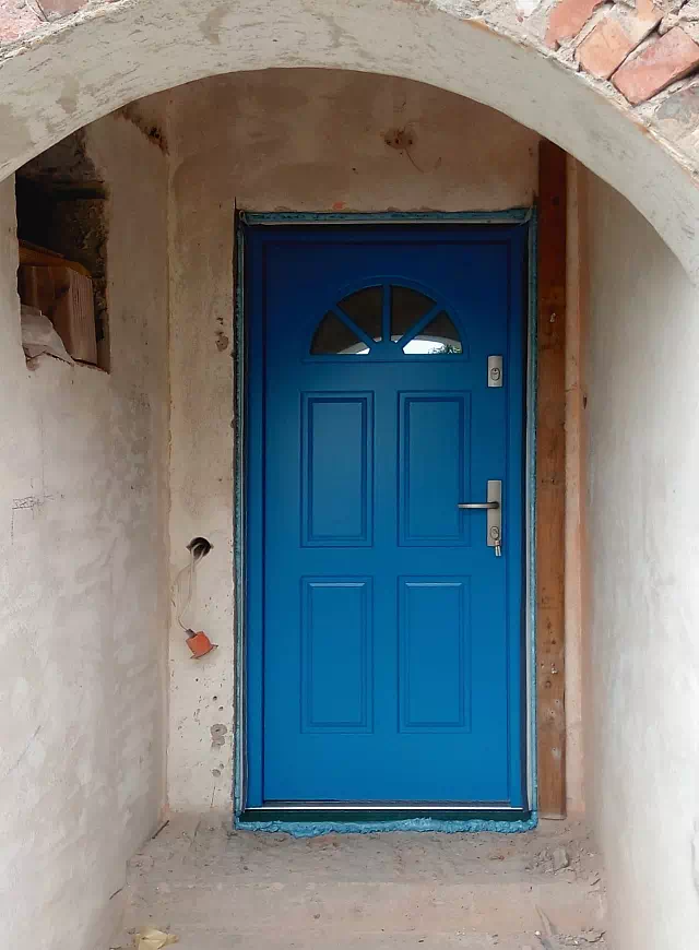 Widok elewacji domu z zamontowanymi drzwiami wzór 506,2 wymalowanymi w kolorze niebieskie.