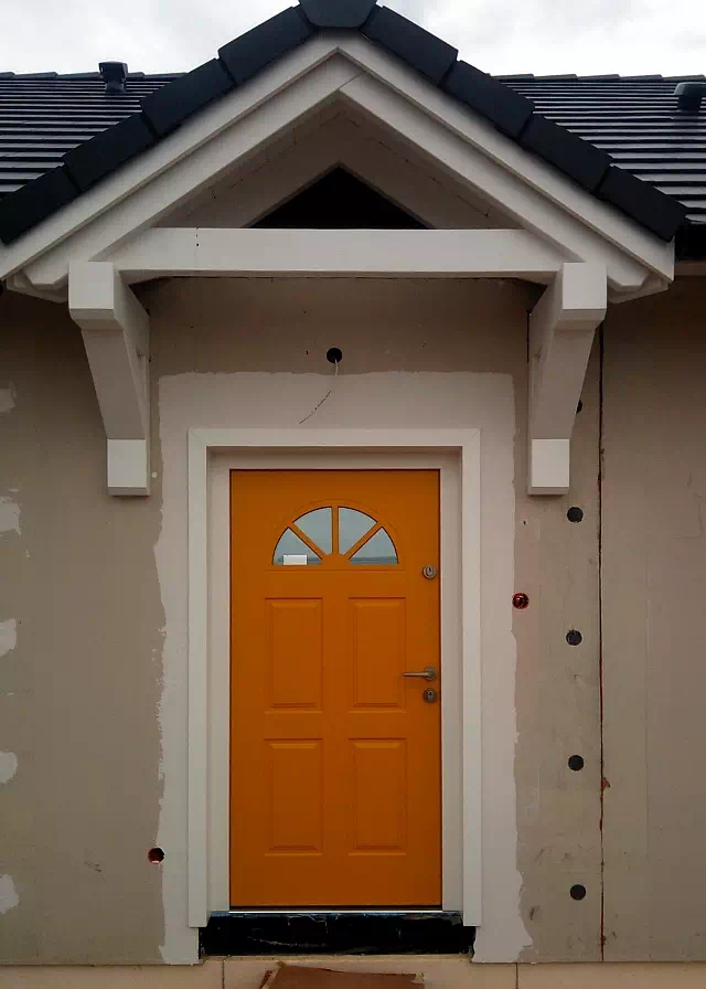 Widok elewacji domu z zamontowanymi drzwiami wzór 506,2 wymalowanymi w kolorze pomarańczowe.