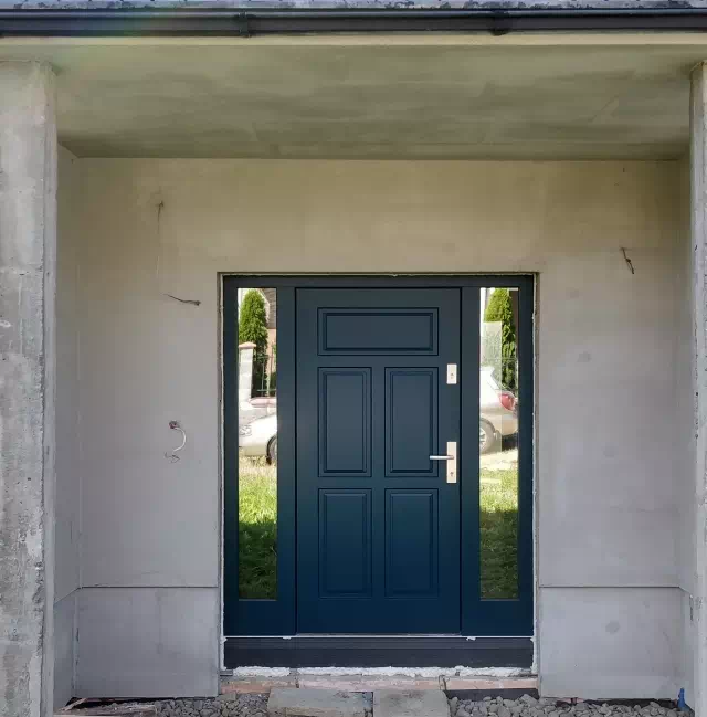 Widok elewacji domu z zamontowanymi drzwiami wzór 533,11 wymalowanymi w kolorze granatowe.