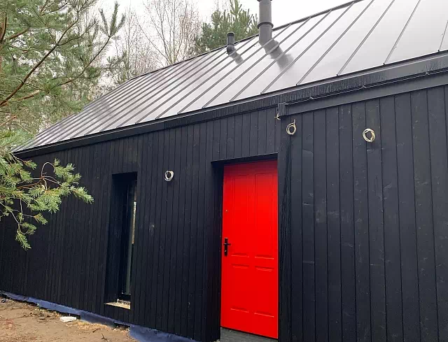 Widok elewacji domu z zamontowanymi drzwiami wzór 534,9 wymalowanymi w kolorze czerwone.