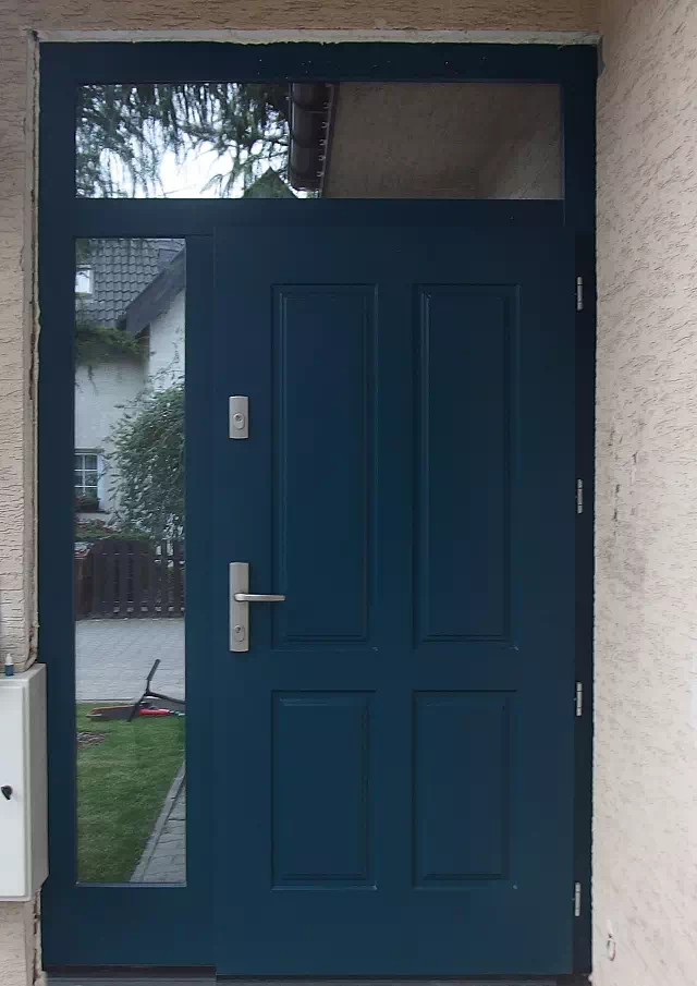 Widok elewacji domu z zamontowanymi drzwiami wzór 534,9 wymalowanymi w kolorze niebieskie.
