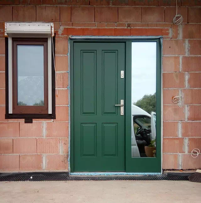 Widok elewacji domu z zamontowanymi drzwiami wzór 534,9 wymalowanymi w kolorze zielone.