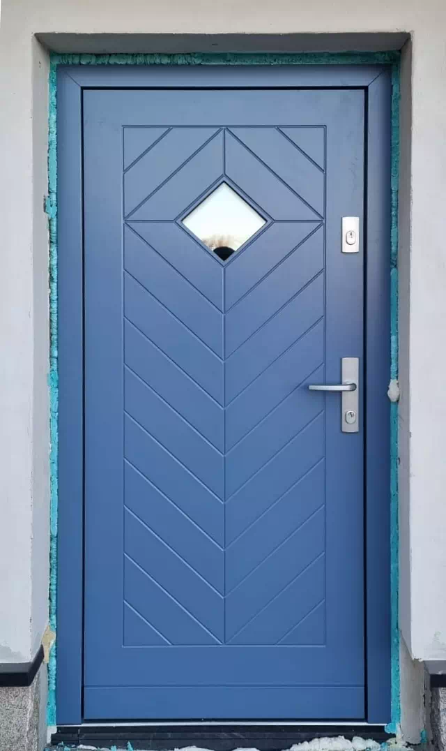 Widok elewacji domu z zamontowanymi drzwiami wzór 543,1 wymalowanymi w kolorze niebieskie.