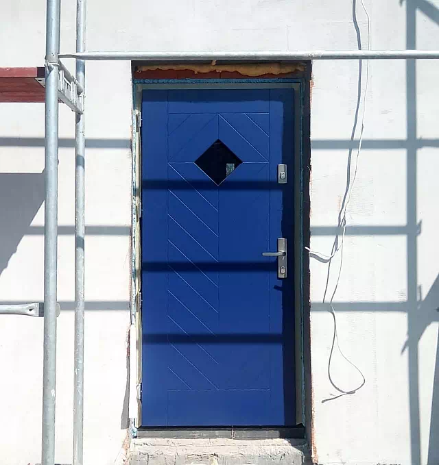 Widok elewacji domu z zamontowanymi drzwiami wzór 543,1B wymalowanymi w kolorze granatowe.