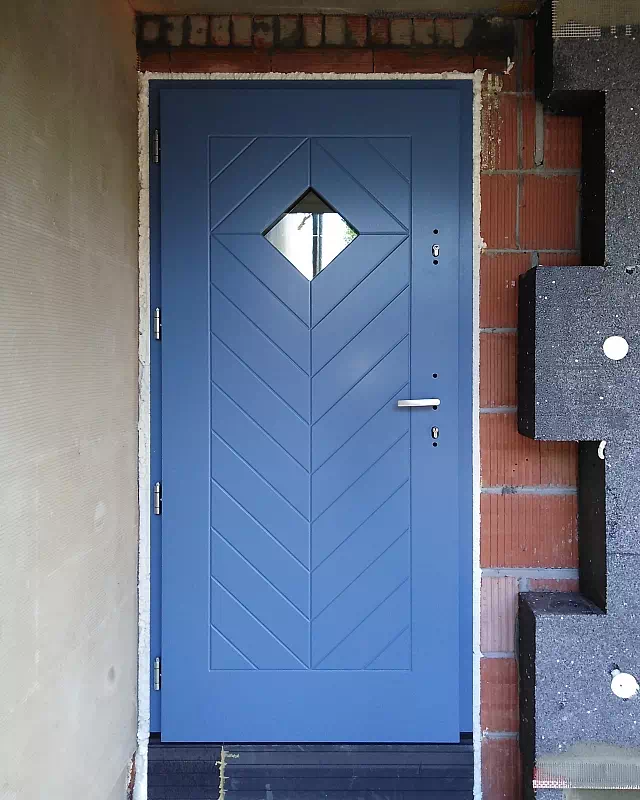 Widok elewacji domu z zamontowanymi drzwiami wzór 543,1C wymalowanymi w kolorze niebieskie.