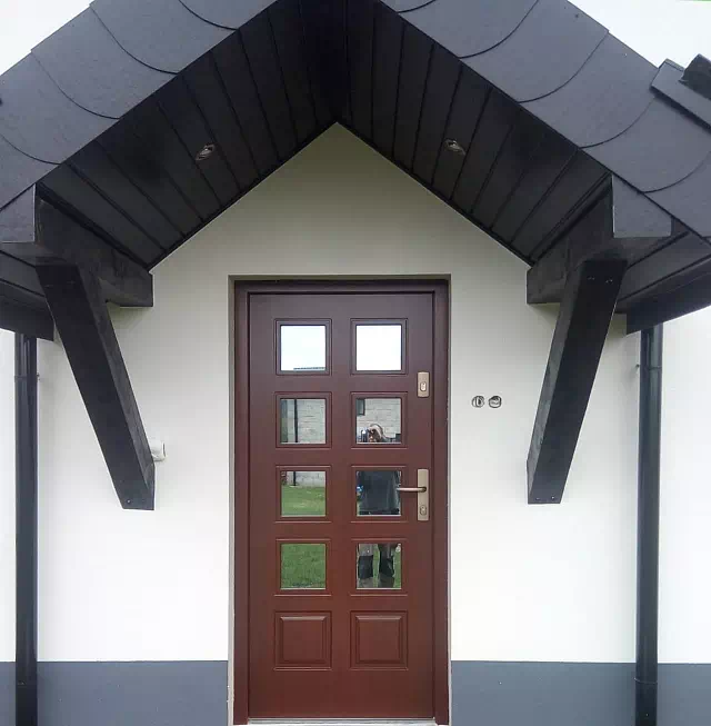 Widok elewacji domu z zamontowanymi drzwiami wzór 574,2 wymalowanymi w kolorze orzech.