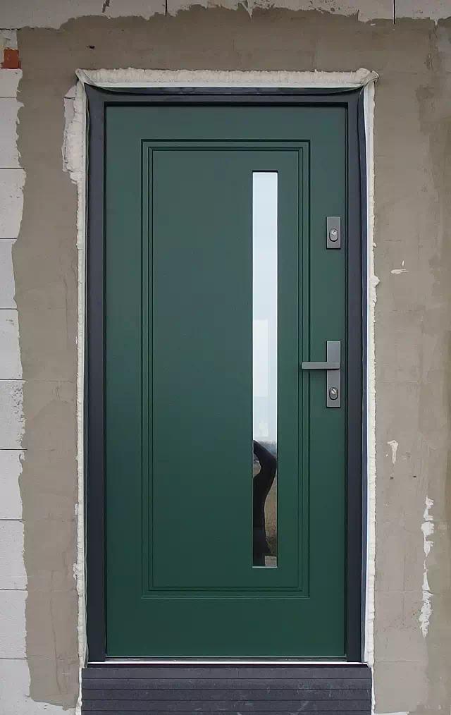 Widok elewacji domu z zamontowanymi drzwiami wzór 577,3b wymalowanymi w kolorze zielone.