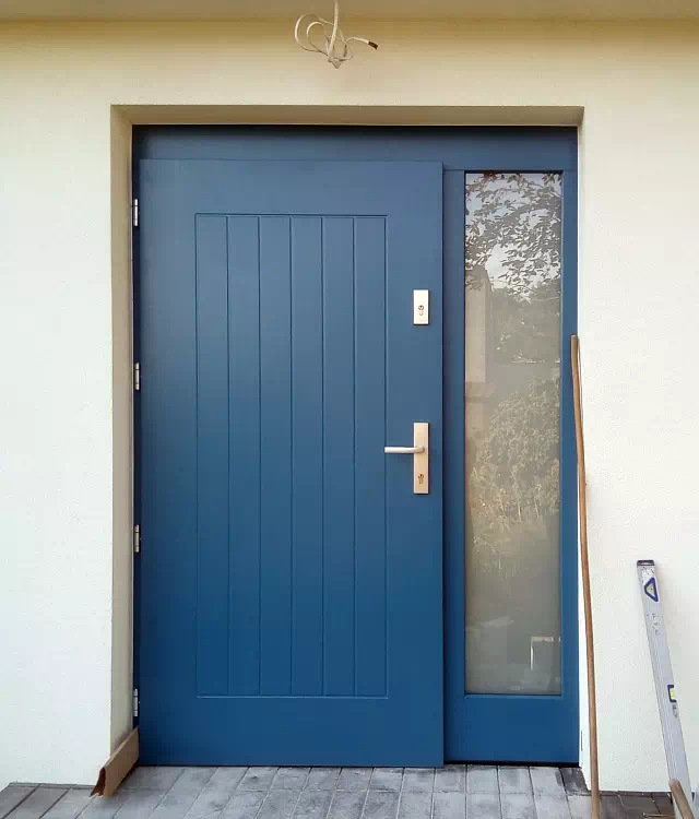 Widok elewacji domu z zamontowanymi drzwiami wzór 688,2 wymalowanymi w kolorze niebieskie.