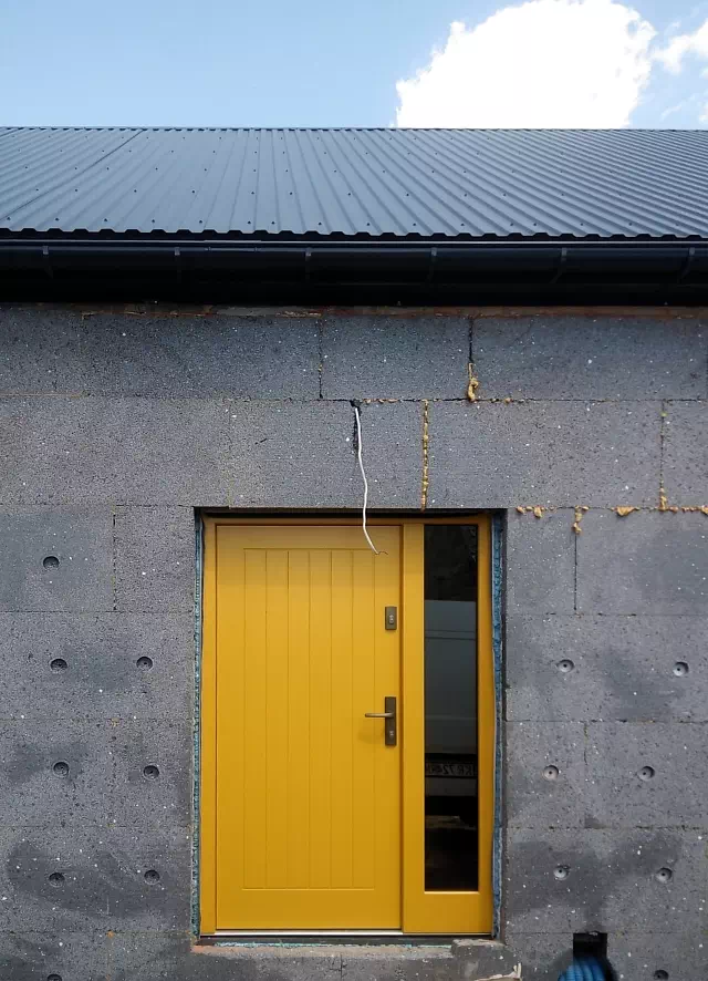 Widok elewacji domu z zamontowanymi drzwiami wzór 688,2 wymalowanymi w kolorze żółte.