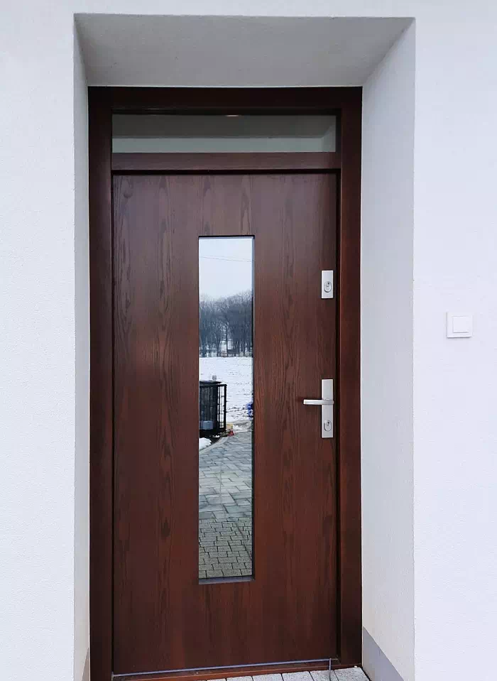 Widok elewacji domu z zamontowanymi drzwiami wzór 499,12 wymalowanymi w kolorze orzech.
