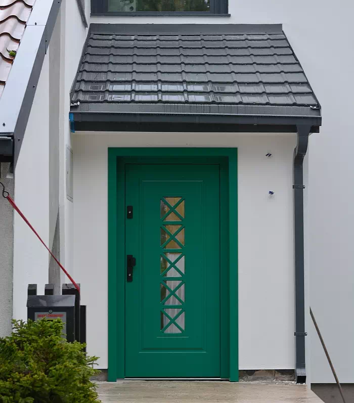 Widok elewacji domu z zamontowanymi drzwiami wzór 546,1 wymalowanymi w kolorze zielone.