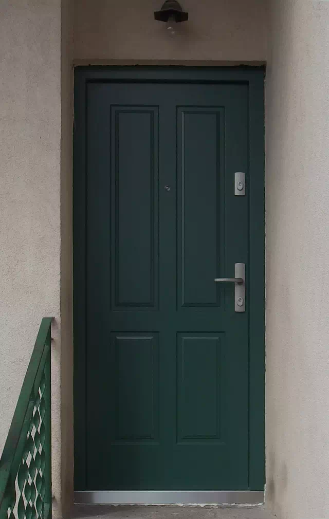 Widok elewacji domu z zamontowanymi drzwiami wzór 534,9 wymalowanymi w kolorze zielone.