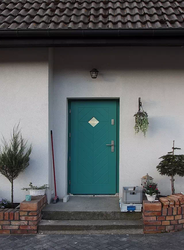 Widok elewacji domu z zamontowanymi drzwiami wzór 543,1 wymalowanymi w kolorze turkusowe.