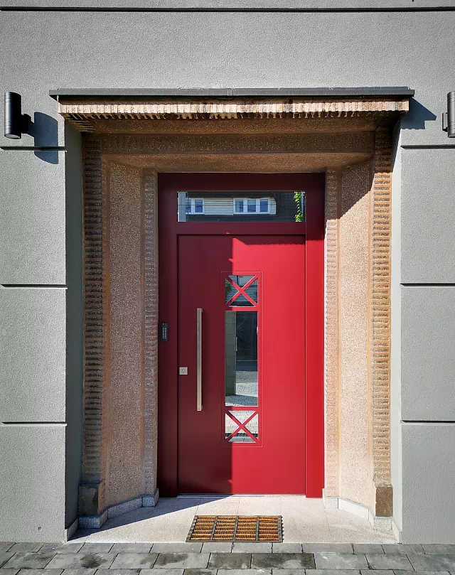 Widok elewacji domu z zamontowanymi drzwiami wzór 461,1 wymalowanymi w kolorze czerwone.