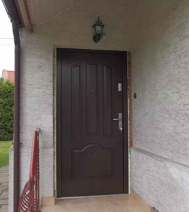 Widok elewacji domu z zamontowanymi drzwiami wzór 502,1+d1 wymalowanymi w kolorze orzech.