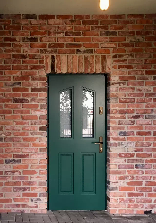 Widok elewacji domu z zamontowanymi drzwiami wzór 534,1 wymalowanymi w kolorze zielone.