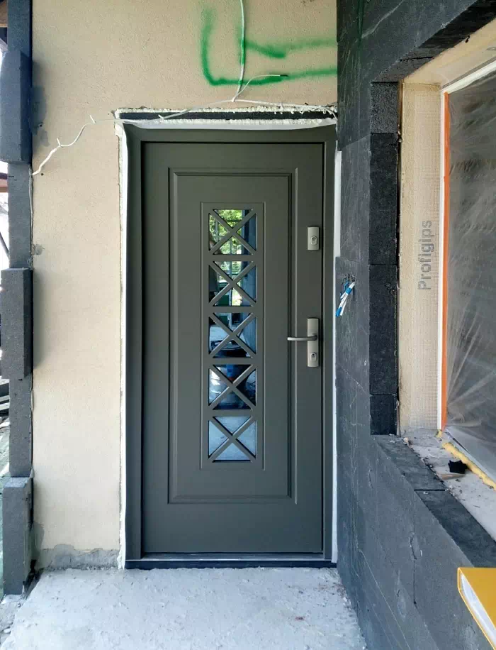 Widok elewacji domu z zamontowanymi drzwiami wzór 546,1 wymalowanymi w kolorze grafitowo-zielone.