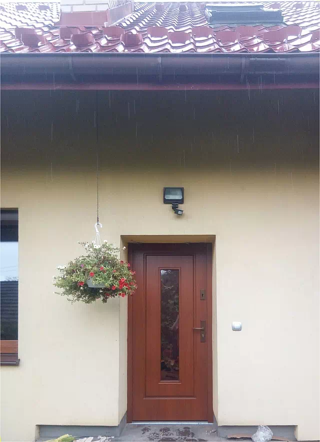 Widok elewacji domu z zamontowanymi drzwiami wzór 572s2 wymalowanymi w kolorze teak.