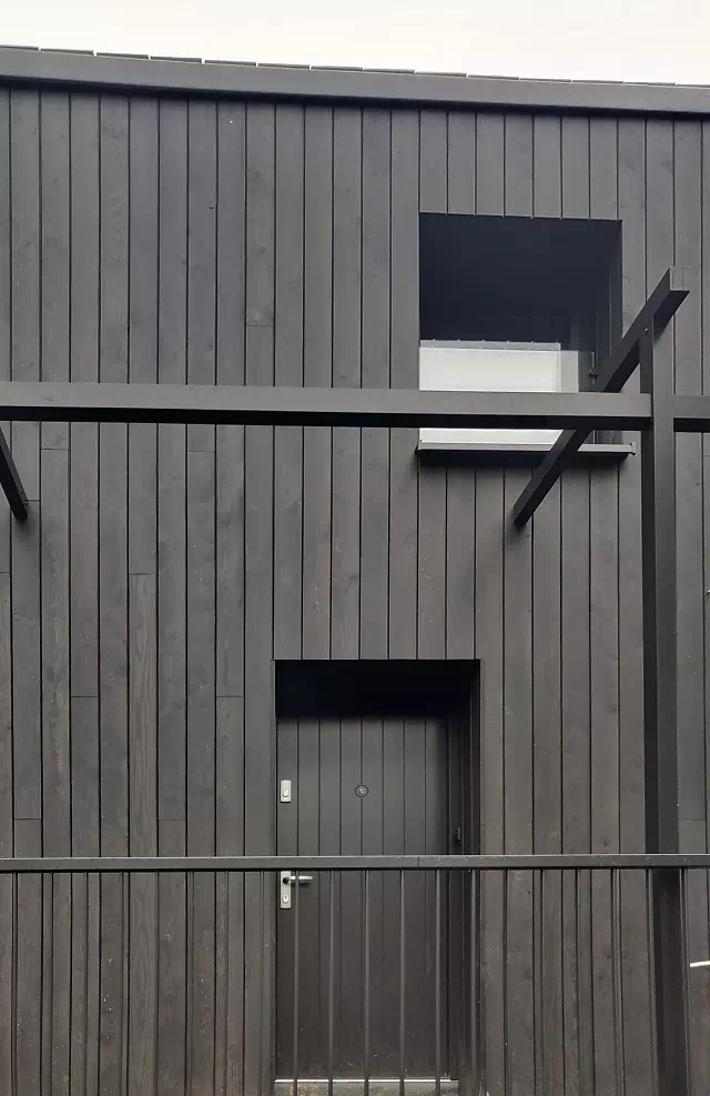 Widok elewacji domu z zamontowanymi drzwiami wzór 689,7w wymalowanymi w kolorze czarne.
